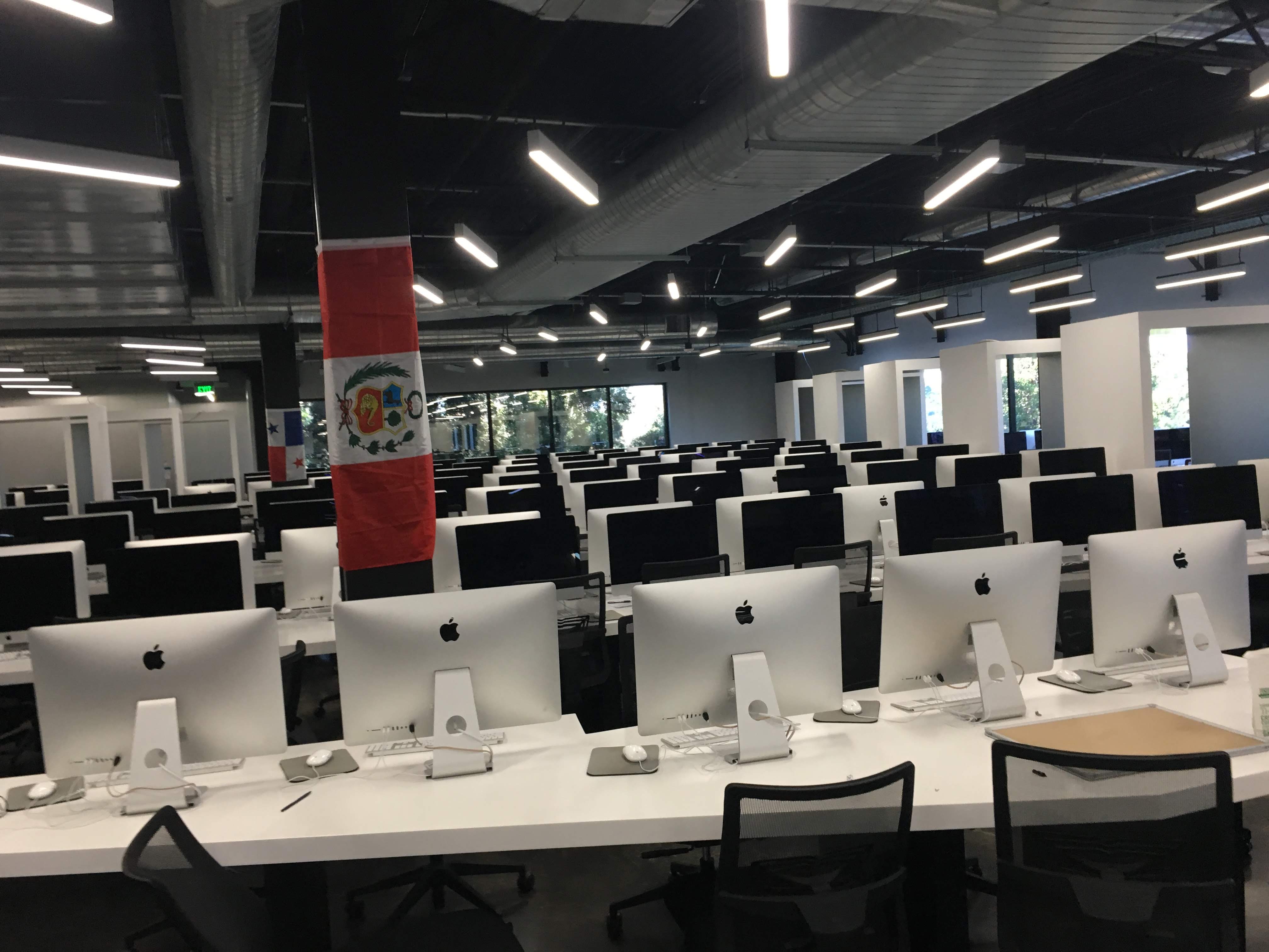 Опенспейс стартапа: ряды iMac на белых столах, с колонны свисают флаги Перу и Панамы
