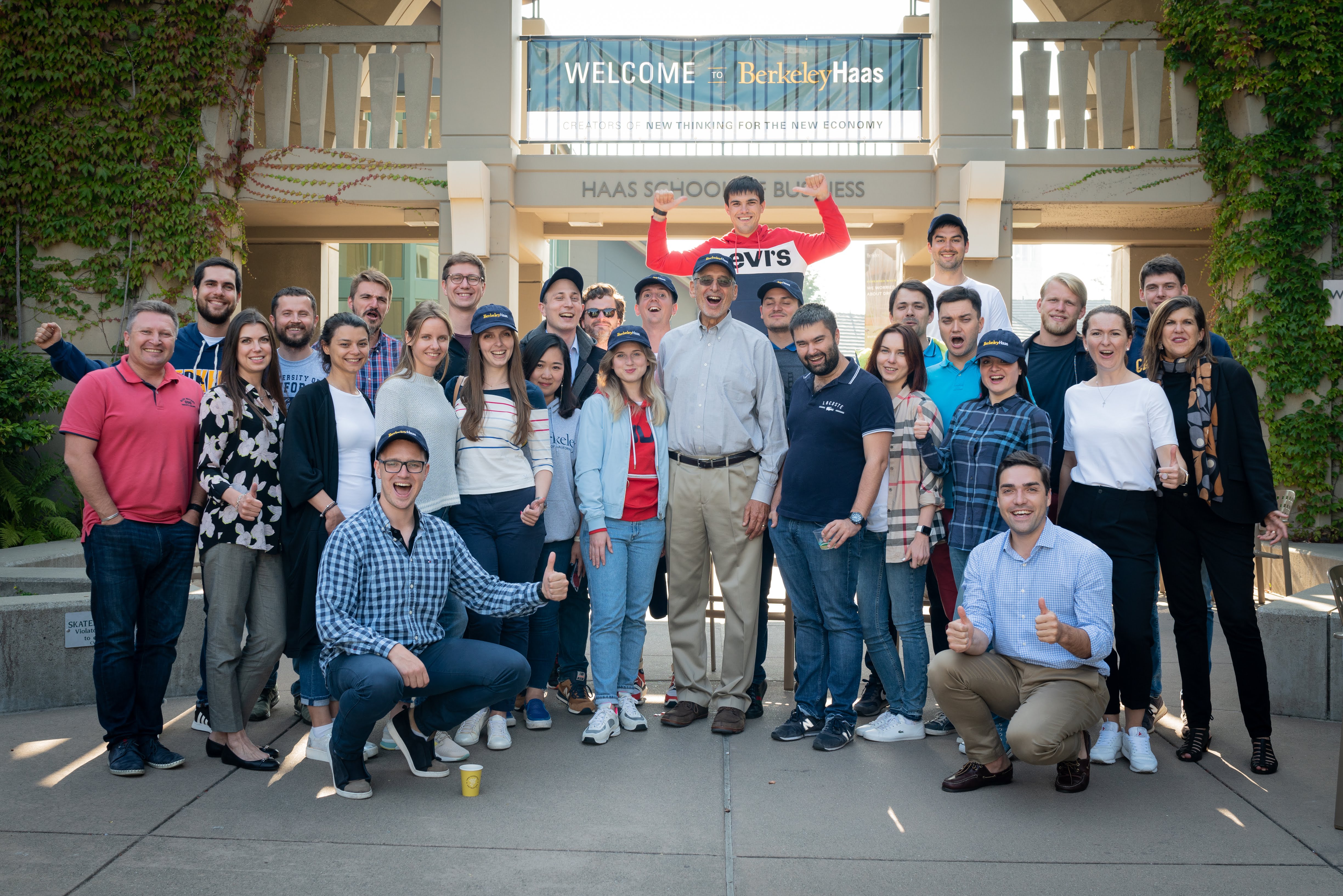Групповое фото участников под баннером Welcome to Berkeley Haas, парень в кепке показывает большой палец