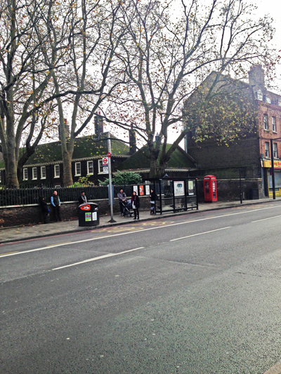 London street with a bus shelter, red telephone box and bare autumn trees beside a brick wall