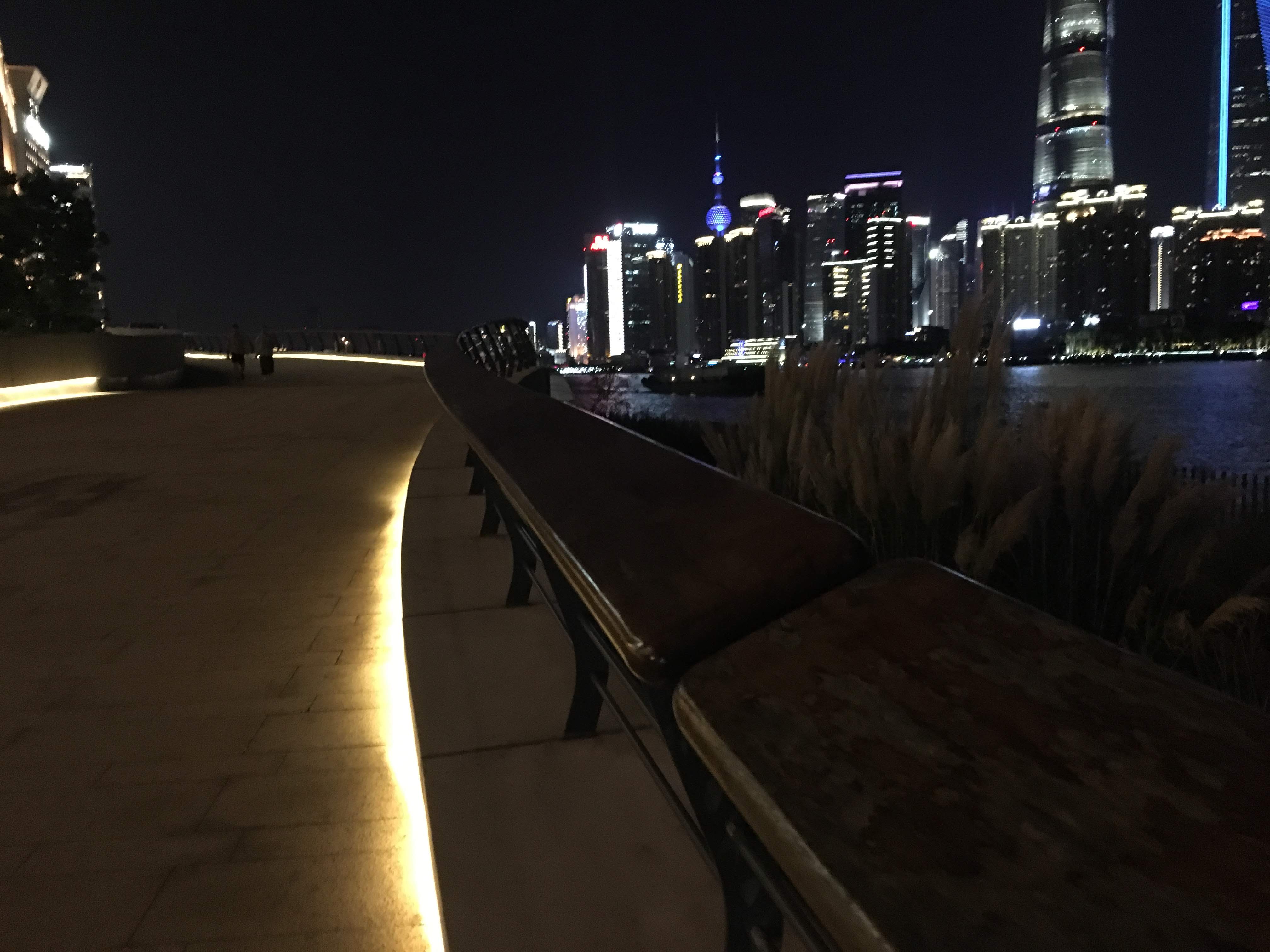 Riverside promenade at night with a bench and the lit Shanghai skyline, including the Oriental Pearl Tower.