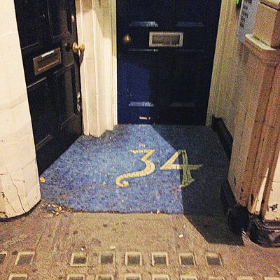 Doorway at night with the number 34 in yellow on a blue floor mat